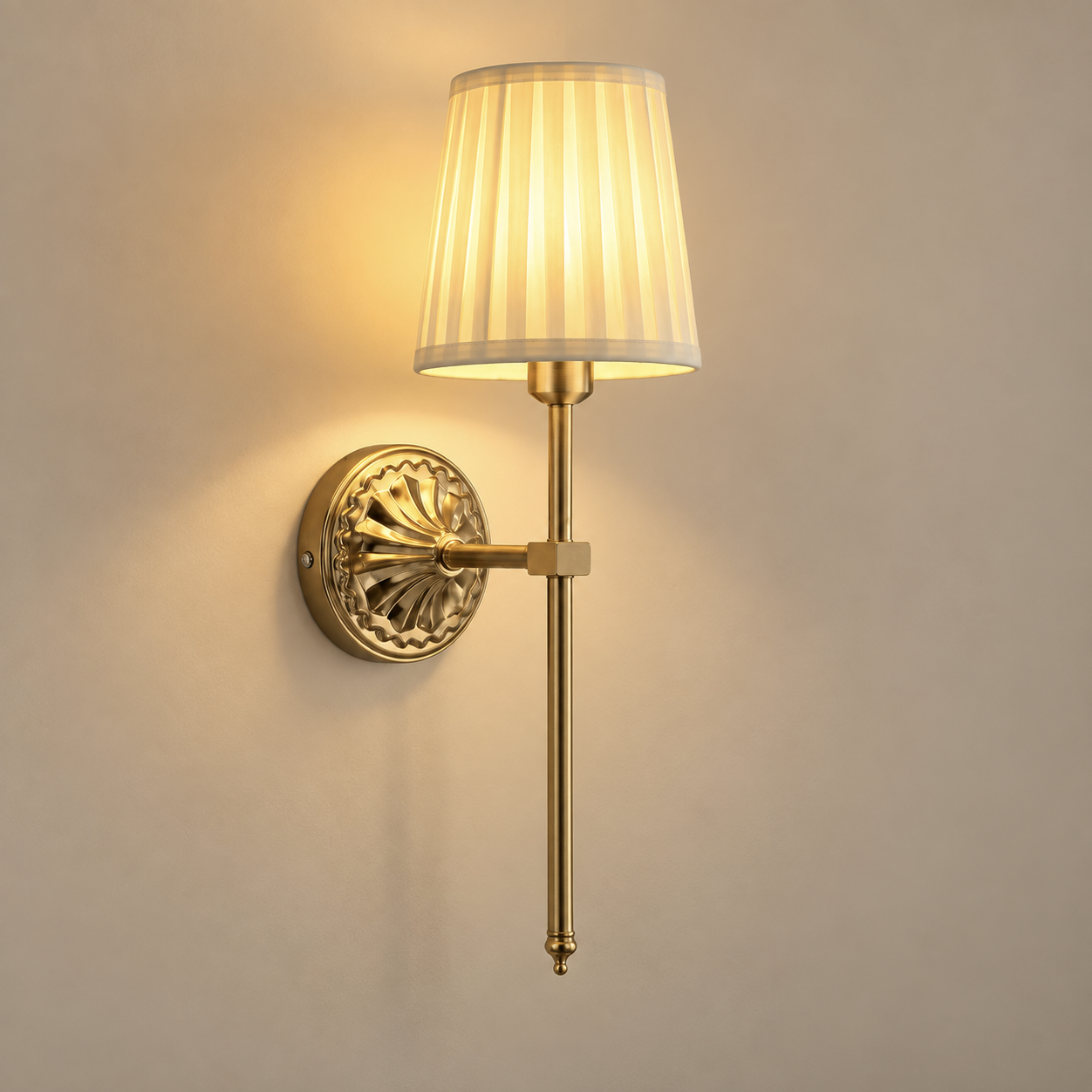 Beatrix cordless rechargeable wall light in antique gold with pleated shade, lit, on a greige wall