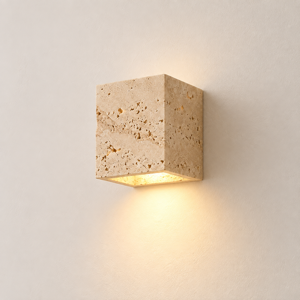 Petra travertine cube wall light, lit, on a warm plaster wall