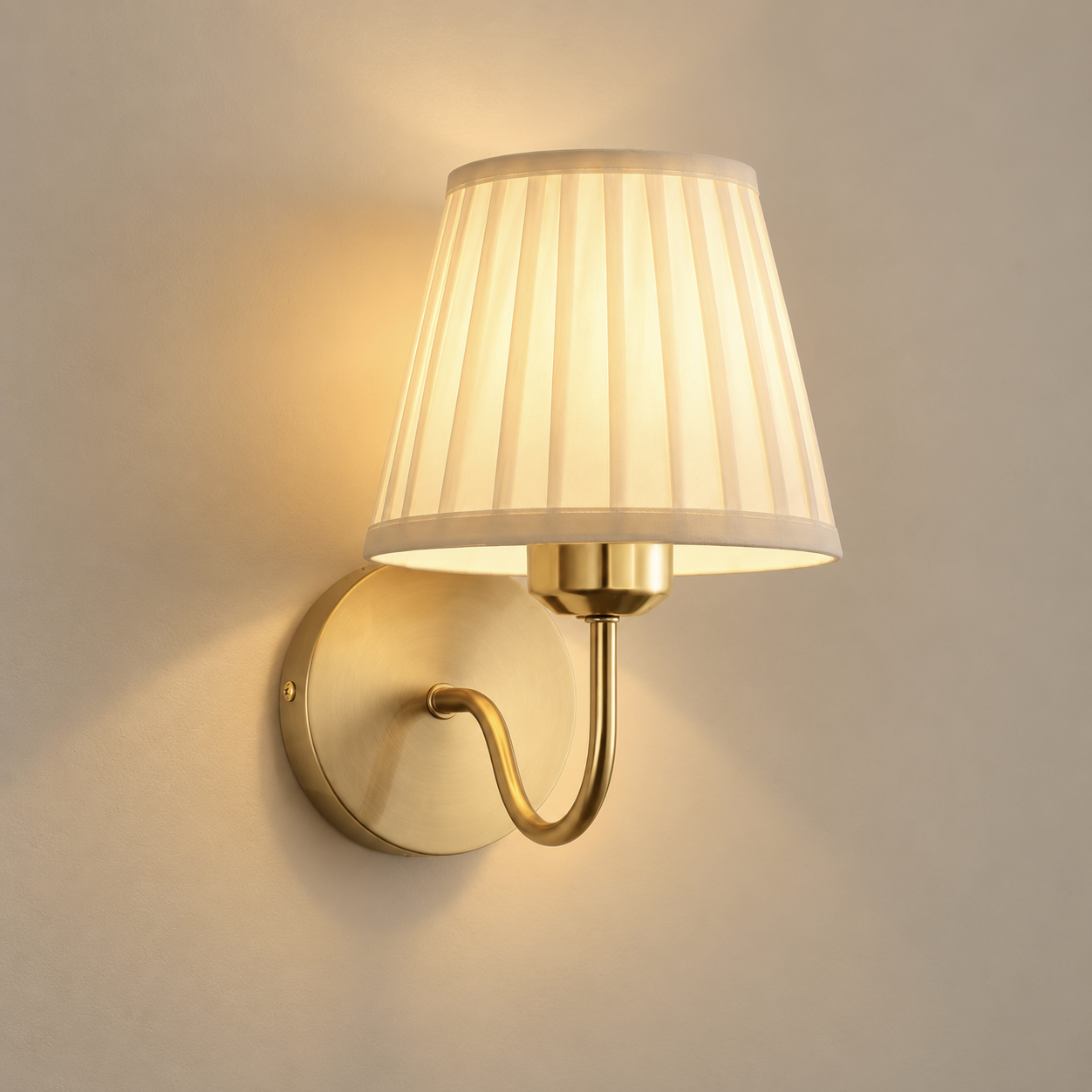 Rosalie cordless rechargeable pleated wall light in brushed gold, lit, on a greige wall